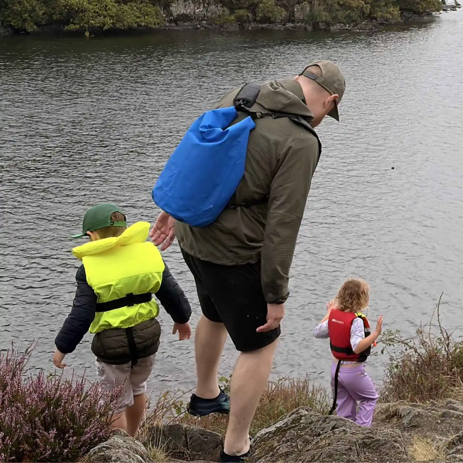 A parent helping two children safely enter the water during a family outdoor trip